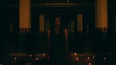 a woman in a black dress and robe standing in the middle of the darkness with a very scary expression while performing a devil worship ritual at night