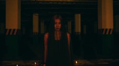 a woman in a black dress and robe standing in the middle of the darkness with a very scary expression while performing a devil worship ritual at night