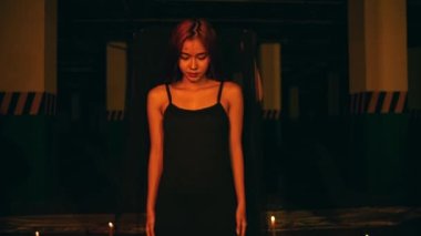 a woman in a black dress puts on a black robe while performing a devil worship ritual in the dark at night