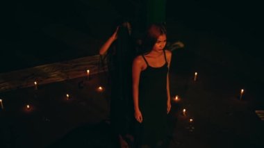 Siyah elbiseli bir kadın gece karanlığında şeytana tapma ayini yaparken siyah bornoz giyer.