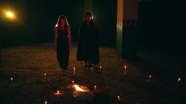 a group of satanic cultists walk amidst an altar of pentagrams and lit candles during a ritual at night