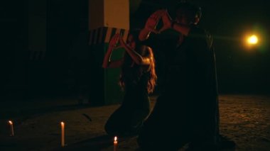 a couple of devil worshipers in black robes are performing a satanic worship ritual by dancing in the middle of a pentagram altar at night