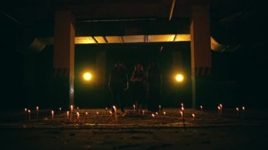 Siyah cüppeli bir grup satanist bir akşam ayini sırasında üç köşeli pentagram şeklinde mumların arasında yürürler.
