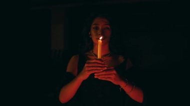 a woman performs a satanic ritual movement with a lit candle in the dark at night