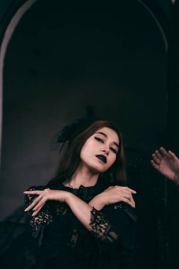 a gothic Indonesian woman wearing a beautiful black hat while dressing like a witch in black at a funeral