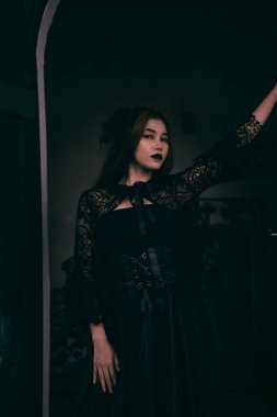 a goth Asian woman dresses up with black make up and wears black clothes like a scary woman at the funeral in the morning
