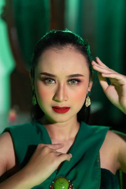 a beautiful Asian woman in a green dress is posing with her hands very gracefully and has green eyes and black hair