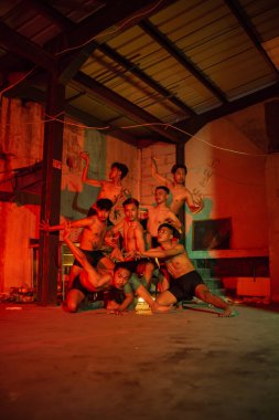 a group of men without clothes dancing poses in an old building with a red light at night