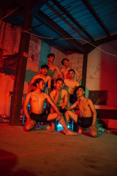 a group of men without clothes dancing poses in an old building with a red light at night