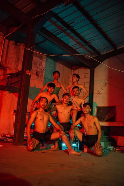 a group of men without clothes dancing poses in an old building with a red light at night