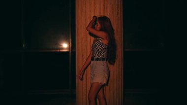 Asian girl with blonde hair and sexy clothes standing in front of a big pillar while waiting for her friends in a bar at night