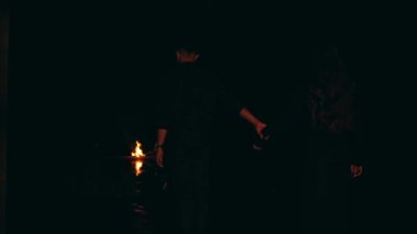 a couple walking towards a bonfire in black clothes in a dark place at night