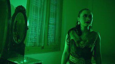 an Asian female dancer stands staring at a mirror with a sorry expression alone in her green room