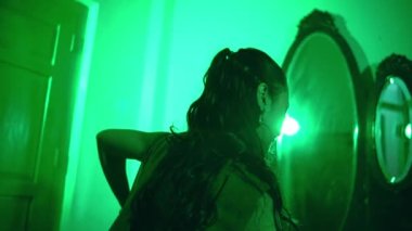 an Asian female dancer dancing in a very sexy dress in front of a mirror in a green room