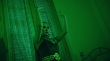 an Asian female dancer dancing in a very sexy dress in front of a mirror in a green room