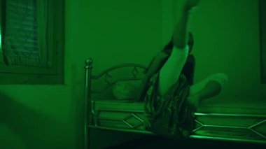 an Asian female dancer dances in a green room with a very sad expression at night