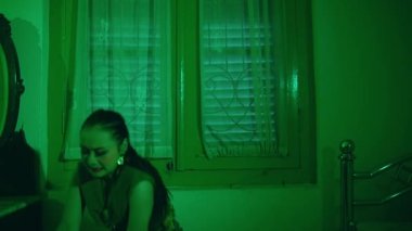 an Asian female dancer dances in a green room with a very sad expression at night