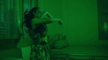 an Asian female dancer dances in a green room with a very sad expression at night