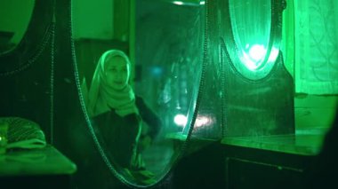 Müslüman bir kadın yeni kıyafetlerini aynanın önünde dener ve yeşil bir odada büyük bir neşeyle giyinir.
