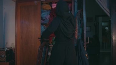 a Muslim woman was cleaning up dirty clothes that were scattered on the bed in her room