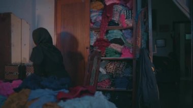 a Muslim woman was cleaning up dirty clothes that were scattered on the bed in her room