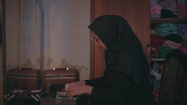 Müslüman bir kadın sabahleyin kahverengi makyaj masasının önündeki makyaj malzemelerini temizliyor.