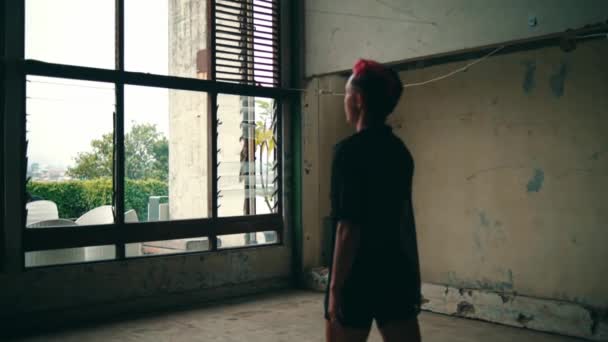 窓の前に赤い髪と黒いシャツを着た美しいアジアの若者 — ストック動画