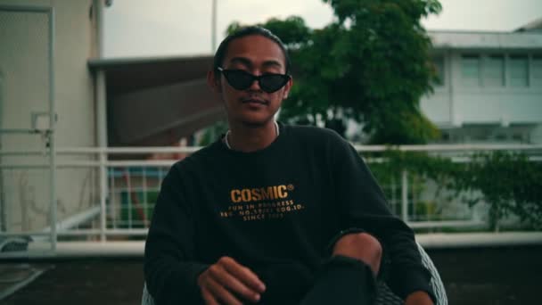 Retrato Jovem Asiático Óculos Pretos Uma Camiseta Preta Sentada Uma — Vídeo de Stock