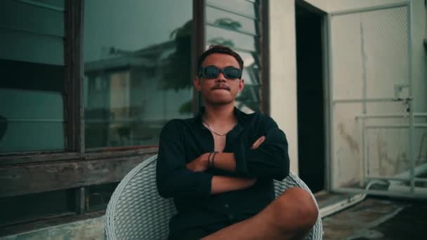 Portret Młodego Azjaty Okularach Przeciwsłonecznych Siedzącego Krześle Podczas Oglądania Kamery — Wideo stockowe