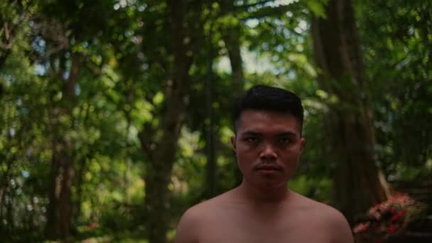 森の中のカメラを見ながら 裸の胸を持つ若いアジア人男性の肖像画 顔に集中しろ フィールドの浅い深さ — ストック動画