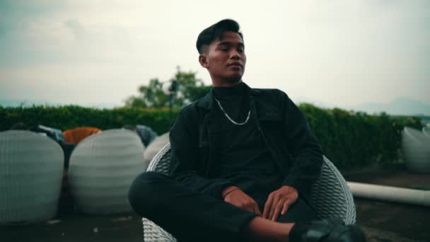 Portret Młodego Azjaty Czarnej Kurtce Łańcuszku Siedzącego Krześle Podczas Relaksu — Wideo stockowe