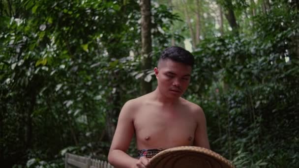 森の真ん中に怒りの表情で橋の端に座って胸を開いているアジア人の男 — ストック動画