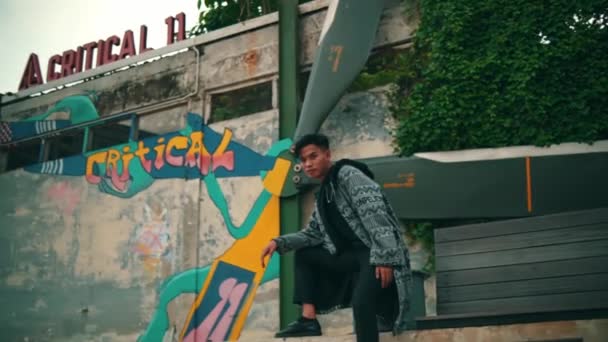 Azjata Wzorzystym Szlafroku Czarnych Spodniach Pozuje Stylowo Przed Ścianą Graffiti — Wideo stockowe