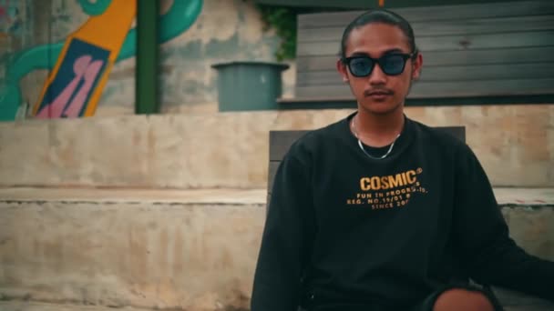 Seorang Pria Asia Dengan Celana Robek Dan Sweater Hitam Duduk — Stok Video