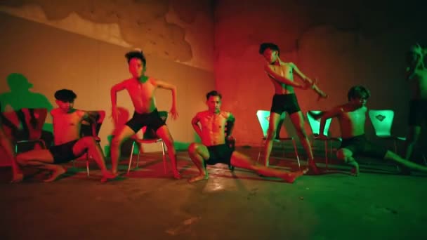夜にネオンの短いボクサーを着て暗い部屋で一緒に踊るアジアの男性のグループ — ストック動画