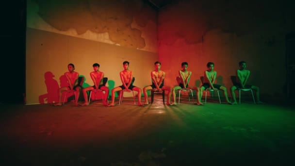 夜の間 赤と緑のライトの部屋の椅子に座っている若者のグループ — ストック動画