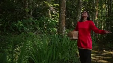 Endonezya, Bali 'de panoramik manzaralı kırmızı yağmurluklu genç bir kadın ormanda yürüyor.