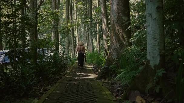 熱帯雨林の道を歩いてわら帽子をかぶったアジア人の男 バックビュー — ストック動画