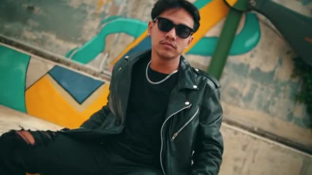 Seorang Pria Asia Dengan Jaket Kulit Dan Kacamata Hitam Duduk — Stok Video