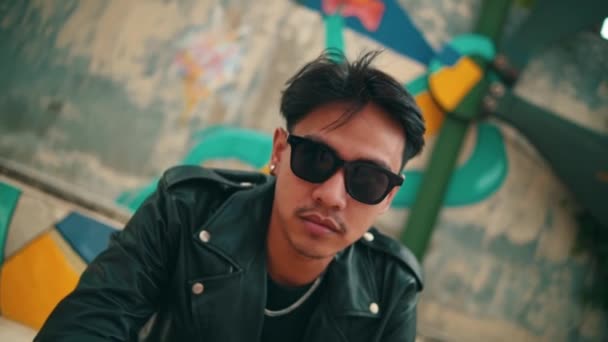 Asiatisk Man Skinnjacka Och Solglasögon Sitter Framför Färgglad Graffiti Vägg — Stockvideo