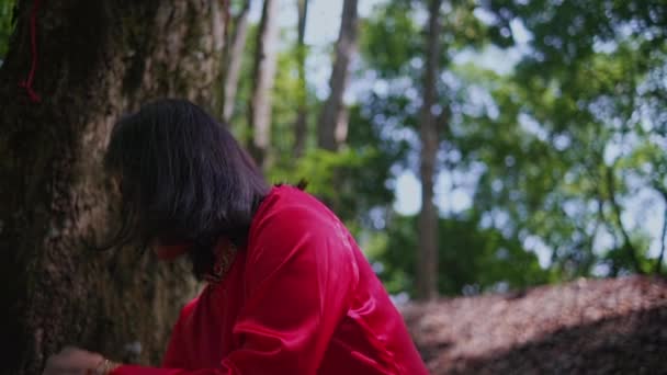 森の木の幹に立つ赤いシャツのアジアの女性とジャングルの中のほうきで葉の多くを掃除 — ストック動画