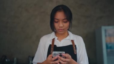 Kafe mutfağında elinde üzgün bir ifadeyle akıllı bir telefon tutan bir kadın.