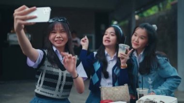 Bir grup Asyalı genç, bir kafede arkadaşlarıyla akıllı telefonlarıyla selfie çekiyorlar.