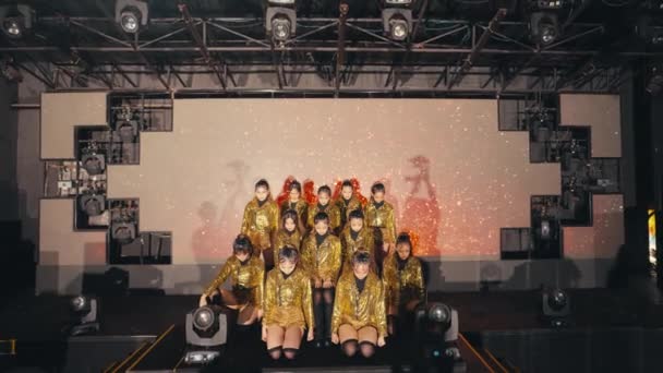 一群亚洲舞蹈家 舞台上穿着金色的服装 后排有一个录象带 — 图库视频影像