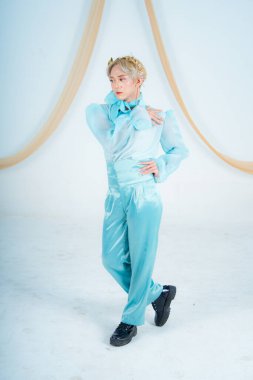 Beyaz bir odada mavi bir kostüm içinde zarif poz veren Asyalı bir kadın.