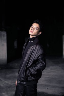 Eski bir binada deri ceket ve siyah pantolon giyen yakışıklı bir Asyalı.