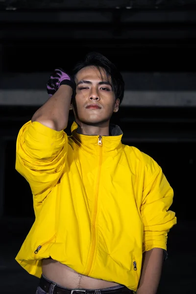 an asian man with a yellow jacket and black hair posing very gallantly in an abandoned building