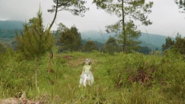 Beyaz kostümlü güzel bir kadın sabah çalılarla dolu bir dağda yürüyor.