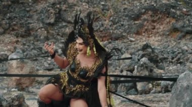 Dramatik tüylü kostümlü güçlü bir cadı sihirli siyah kurdelelerle mücadele ediyor ve onu bir taş çemberin içine bağlıyor. Sahne yoğun duygu, mücadele ve kayalık bir arazide karanlık fantezilerle dolu..