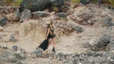 Kayalık bir arazide yürürken zarif bir kraliçeyi takip eden bir çekim. Kamera elbisesinin dalgalı siyah trenine ve kostümünün karmaşık detaylarına ve yandan ve arkadan uzun örgülere odaklanıyor..